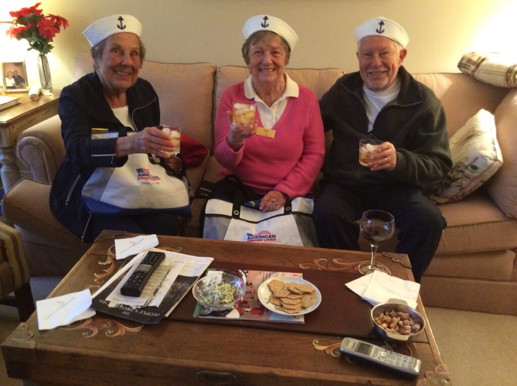 Three senior residents sit on a couch and smile with cocktails in hand.