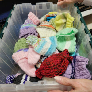 A container full of colorful knitted hats created by the Stitch Wits club at Trillium Woods.