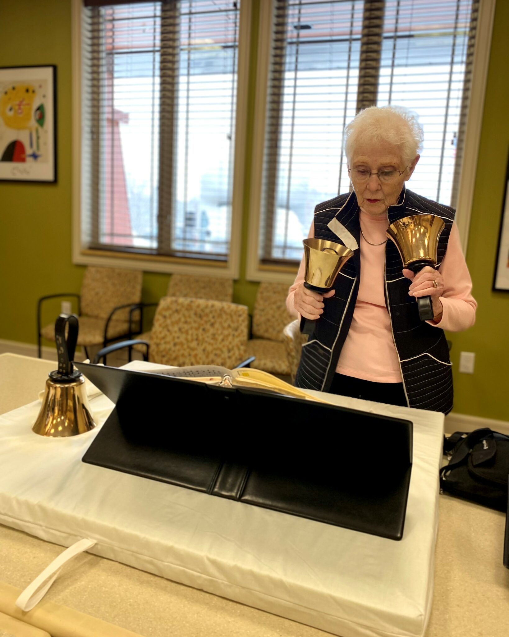 A senior woman looks at her sheet music while holding hand bells, working as part of the Trillium Bells group