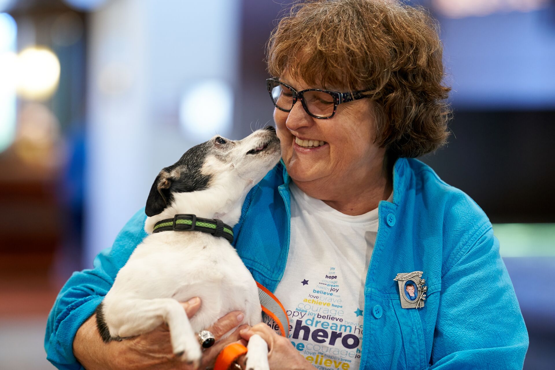 A senior resident gets puppy kisses from a white and brown dog she is holding.