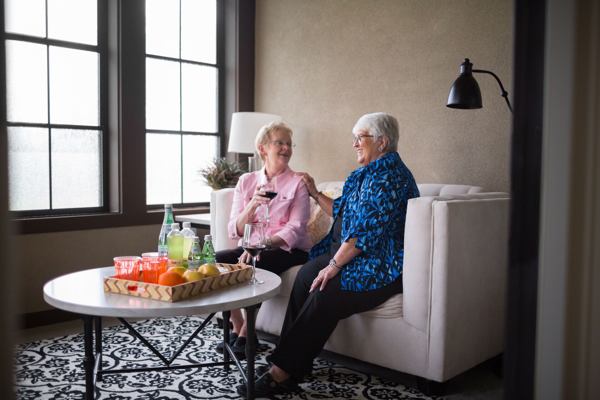 Two senior women sit and visit over drinks.